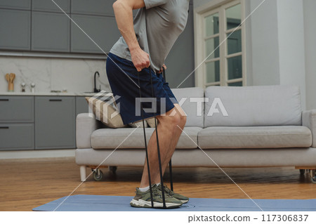 Training to become the best. Beautiful young man in sports clothing exercising at home. 117306837