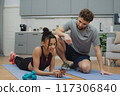 Training to become the best. Beautiful young woman and man in sports clothing exercising at home. 117306840