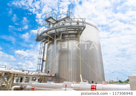 A huge metal tank at a production facility surrounded by pipes 117306948