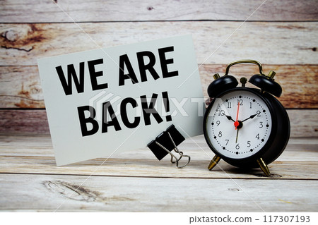 We are Back text on paper card with alarm clock on wooden background 117307193