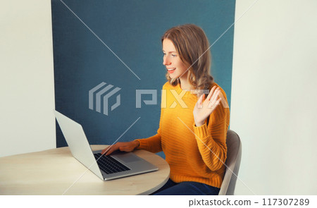 Happy young woman working with laptop welcomes communicates via video call sitting at the desk home 117307289