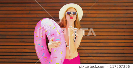 Summer portrait of woman blowing her lips with inflatable ring for swimming wearing straw hat Summer portrait of woman blowing her lips with inflatable ring for swimming wearing straw hat 117307296