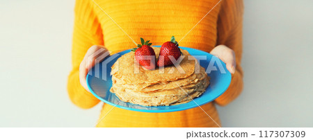 Cooking, close up woman housewife holding plate with stack of pancakes with strawberries 117307309