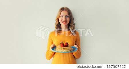 Cooking, happy smiling young woman housewife holding plate with stack of pancakes with strawberries Cooking, happy smiling young woman housewife holding plate with stack of pancakes with strawberries 117307312