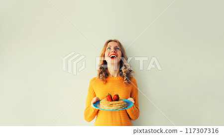 Cooking, happy cheerful young woman housewife holding plate with stack of pancakes with strawberries 117307316