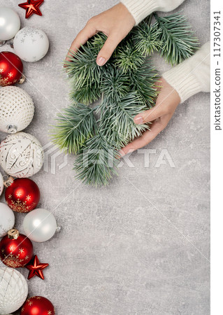 Red and white Christmas baubles in a box flat lay. Merry Christmas and Happy New Year seasons greetings card. Copy space. Festive border hands holding fur tree branch 117307341