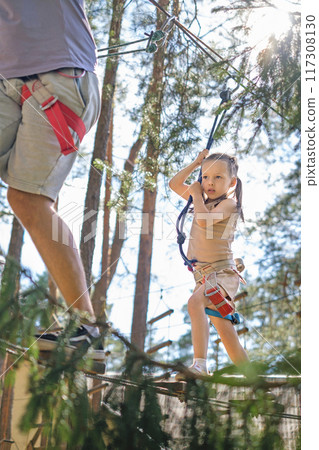 The girl follows her father along a rope route on suspended logs The girl follows her father along a rope route on suspended logs 117308130