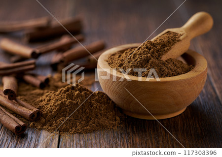 cinnamon powder in a wooden bowl on a dark wooden table, selective focus. cinnamon powder in a wooden bowl on a dark wooden table, selective focus. 117308396