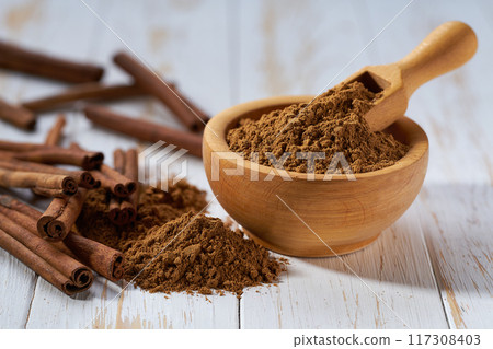 cinnamon sticks and wooden bowl with cinnamon powder on a white wooden table, selective focus. cinnamon sticks and wooden bowl with cinnamon powder on a white wooden table, selective focus. 117308403