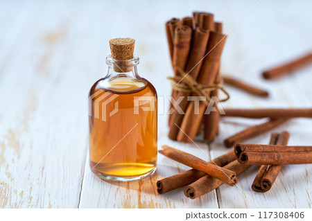 A bottle of essential cinnamon oil with cinnamon sticks on a white wooden table. 117308406