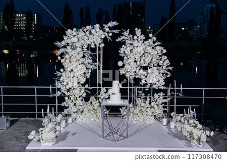 Wedding setup with three-tier white cake with floral accents. Wedding inspiration, luxury events Wedding setup with three-tier white cake with floral accents. Wedding inspiration, luxury events 117308470