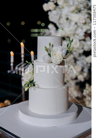 Wedding setup with three-tier white cake with floral accents. Wedding inspiration, luxury events Wedding setup with three-tier white cake with floral accents. Wedding inspiration, luxury events 117308475