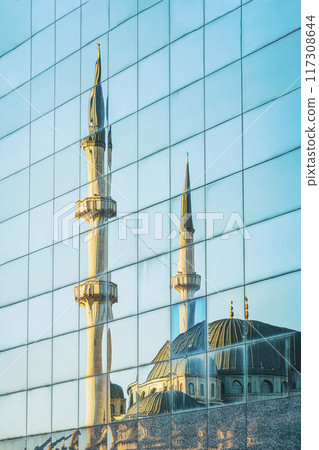 A mosque with minarets is reflected in the glass facade of modern building A mosque with minarets is reflected in the glass facade of modern building 117308644