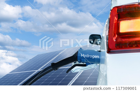 Close up of fuel cell car with connected hydrogen fueling nozzle. Solar panel in the background 117309001