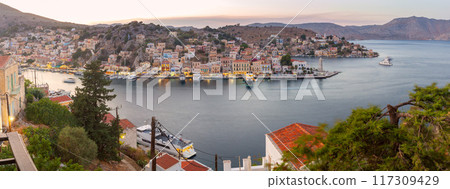 Multi-colored facades of houses in the light of lanterns in the village of Symi at sunset. 117309429