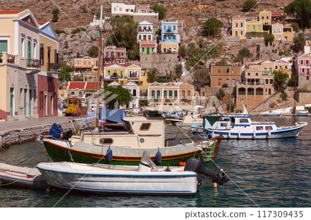 Colourful house facades and fishing boats in the bay of Symi village at sunset. 117309435