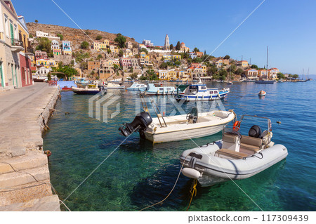 Colourful house facades and fishing boats in the bay of Symi village at sunset. 117309439