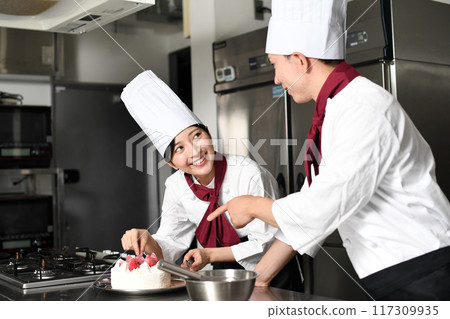 A female pastry chef making a cake and a man teaching her 117309935