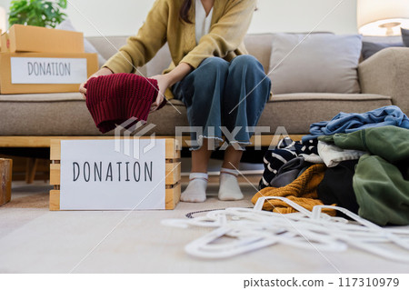 Young Asian women sit in living room sorting clothes for donation in a donation box second hand clothes. Donate concept Young Asian women sit in living room sorting clothes for donation in a donation box second hand clothes. Donate concept 117310979
