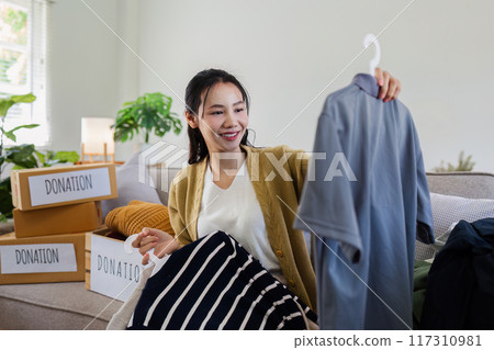 Young Asian women sit in living room sorting clothes for donation in a donation box second hand clothes. Donate concept 117310981