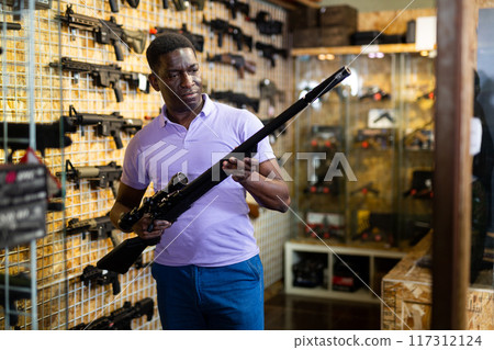 African american man chooses rifle with telescopic sight and silencer African american man chooses rifle with telescopic sight and silencer 117312124