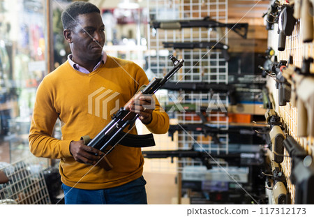 Man choosing assault rifle in arms shop 117312173