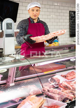 Diligent male butcher offering to sell big piece of beef beef in butcher shop Diligent male butcher offering to sell big piece of beef beef in butcher shop 117312190
