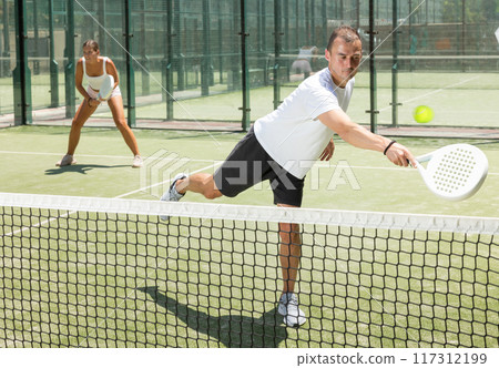 Active woman and man tennis players with rackets playing padel on an court Active woman and man tennis players with rackets playing padel on an court 117312199