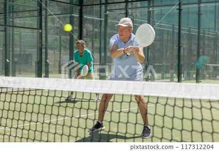 Elderly and adult men playing doubles padel Elderly and adult men playing doubles padel 117312204
