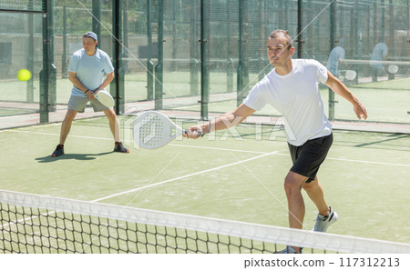 Padel game - man with partners plays on court Padel game - man with partners plays on court 117312213