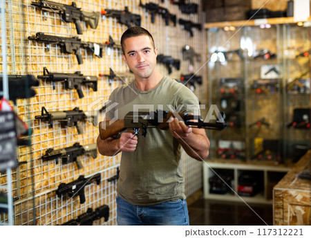 Male shopper chooses pneumatic assault rifle at gun store closeup Male shopper chooses pneumatic assault rifle at gun store closeup 117312221