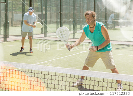 Two adult men playing doubles padel 117312223