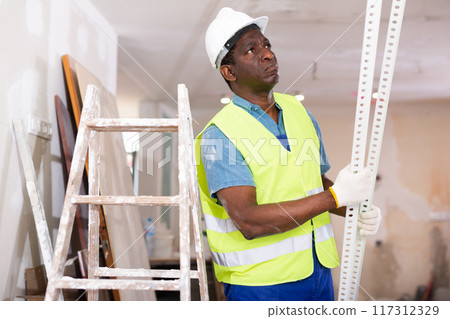 African-american man builder carrying metallic profile while working in room 117312329