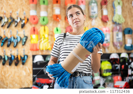 Young girl chooses and buys climbing rope for trip to the mountains in sports equipment store 117312436