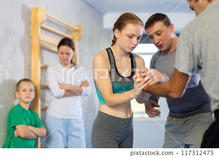 Trainer on man explains palm grab technique, boy, girl and woman watch and learn 117312475