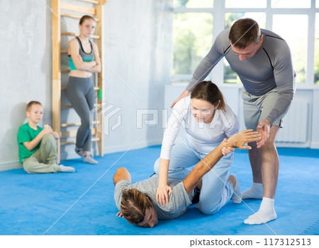 At self-defense training, trainer teaches woman technique of grabbing arm and lowering opponent to floor At self-defense training, trainer teaches woman technique of grabbing arm and lowering opponent to floor 117312513