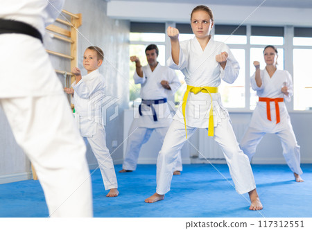 Teen girl with family repeat movements and learn fighting techniques during martial arts lesson Teen girl with family repeat movements and learn fighting techniques during martial arts lesson 117312551