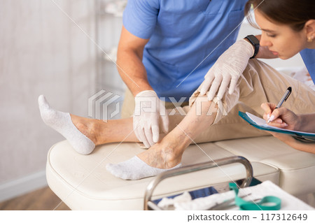 Cropped male doctor shows problem areas of varicose veins on mature woman patients leg. 117312649