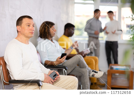 Middle-aged male visitor sitting on chair in waiting hall of clinic 117312658