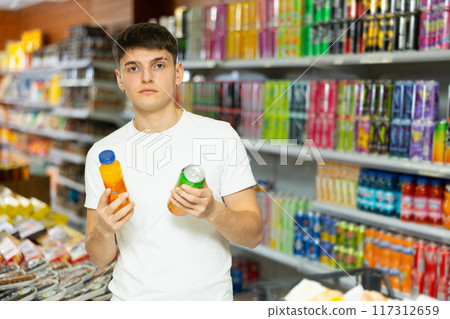 Interested young guy choosing non-alcoholic beverages in supermarket 117312659