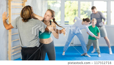 Girl and man in group self-defense classes practicing sparring technique of blowing to chin in gym Girl and man in group self-defense classes practicing sparring technique of blowing to chin in gym 117312718