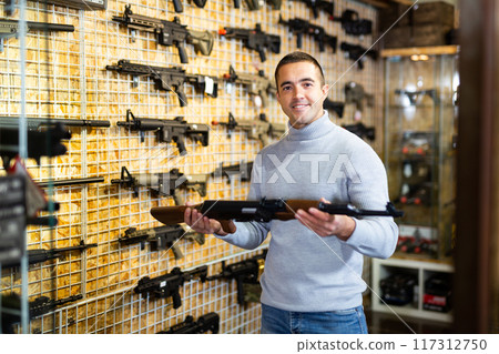 Handsome adult male in hunting shop with rifle in hands Handsome adult male in hunting shop with rifle in hands 117312750