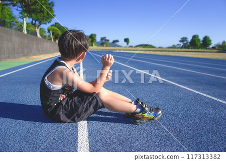 Small boy training for athletics on a blue track on a sunny day Small boy training for athletics on a blue track on a sunny day 117313382