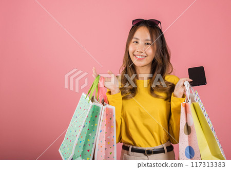 Portrait Asian happy beautiful young woman teen shopper smiling standing excited holding online shopping bags online colorful on mobile phone or smartphone studio shot isolated on pink background Portrait Asian happy beautiful young woman teen shopper smiling standing excited holding online shopping bags online colorful on mobile phone or smartphone studio shot isolated on pink background 117313383