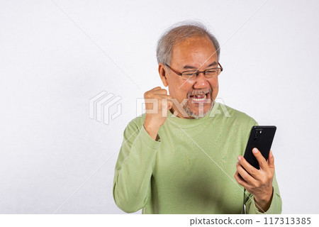 Portrait Asian smiling old man holding a cell phone celebrating something on the phone studio shot isolated on white background, happy senior man doing winner gesture celebrate on mobile phone Portrait Asian smiling old man holding a cell phone celebrating something on the phone studio shot isolated on white background, happy senior man doing winner gesture celebrate on mobile phone 117313385