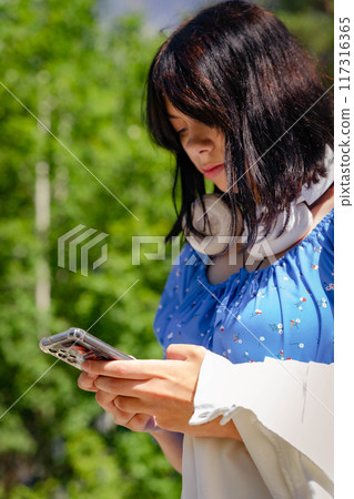 Woman attentively checks her phone surrounded by lush greenery 117316365