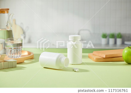 Two white bottles without label displayed on green table with wooden tray, cutting board and glass cup. Behind is kitchen background. Front view 117316761