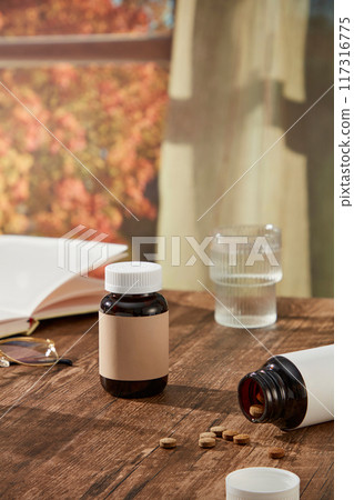 On a wooden table, medicine bottles unlabeled with pills, water cup and notebook decorated. Front view, creative advertisement with space for design 117316775