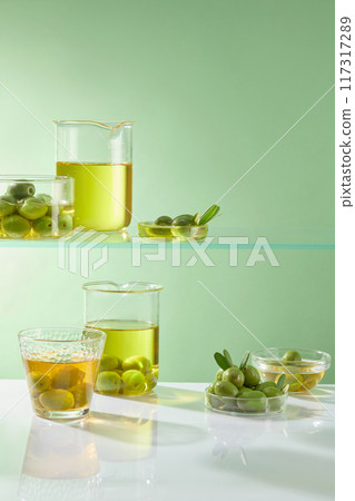 The glass shelves in the laboratory are filled with beakers containing olives and olive oil. Green background with laboratory concept for advertising product. Blank space for presentation The glass shelves in the laboratory are filled with beakers containing olives and olive oil. Green background with laboratory concept for advertising product. Blank space for presentation 117317289