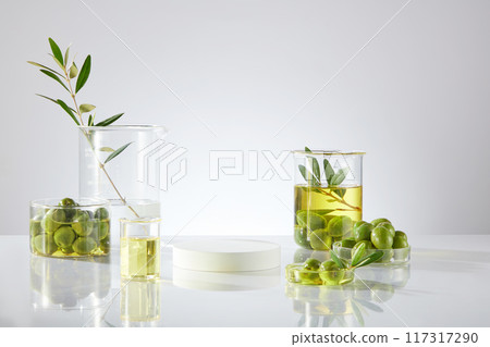 On white table and white background, lab glassware containing fresh olives and olive oil decorated. An empty podium for presentation product. Front view, advertising photo On white table and white background, lab glassware containing fresh olives and olive oil decorated. An empty podium for presentation product. Front view, advertising photo 117317290